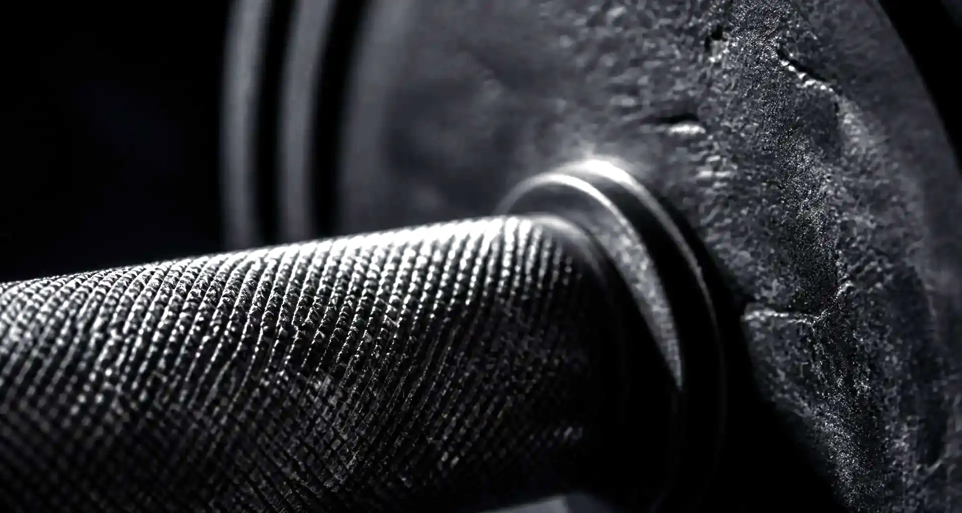 Close-up of the knurling on a barbell with chalk dust, a loaded plate behind it